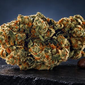 Flor de cannabis con tricomas dorados y naranjas junto a semillas de cacao sobre superficie oscura