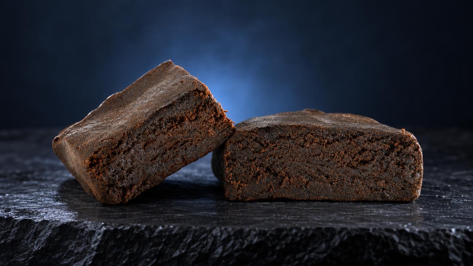 Dos bloques de hachís Kashmir con textura granulosa marrón oscuro, sobre superficie negra