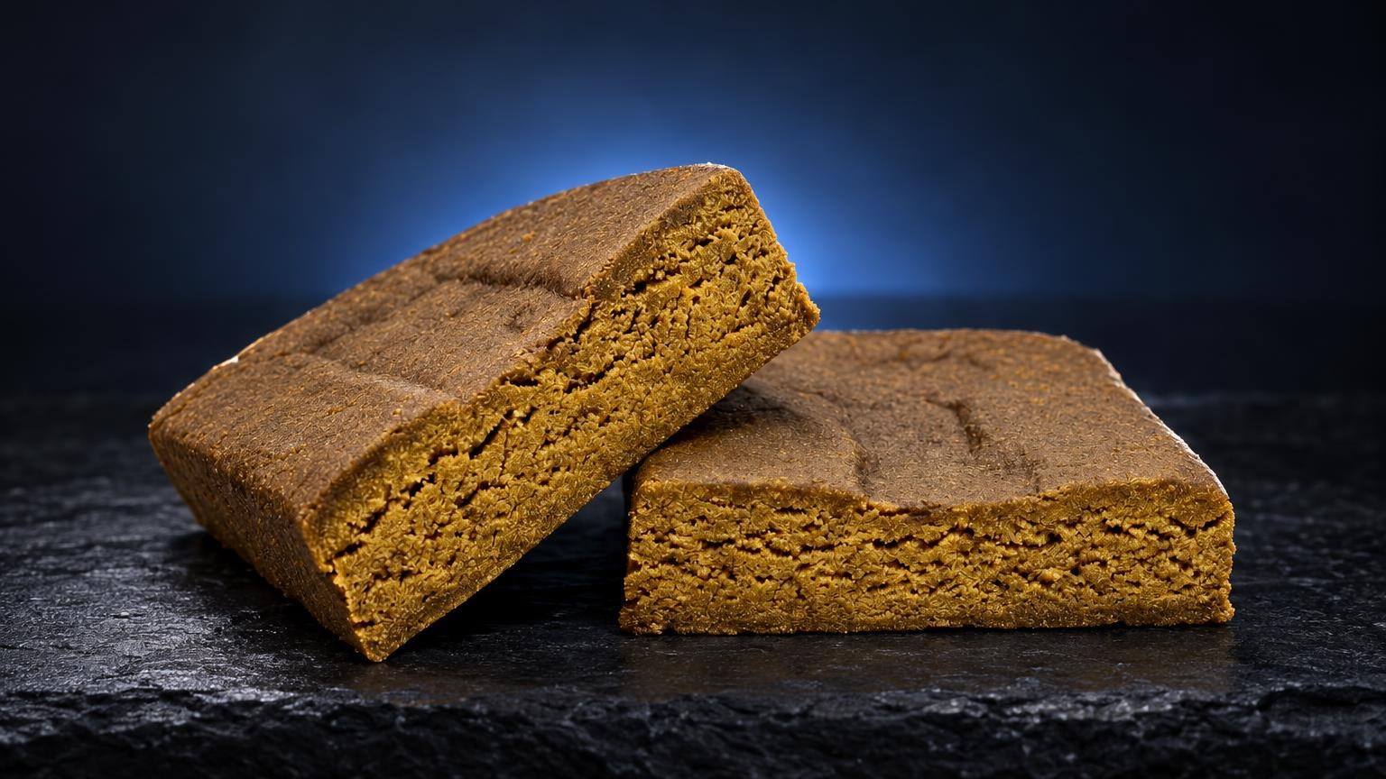Dos bloques de hachís Keta Dream de color amarillo oscuro y textura granulosa sobre superficie negra, ejemplo de static hash